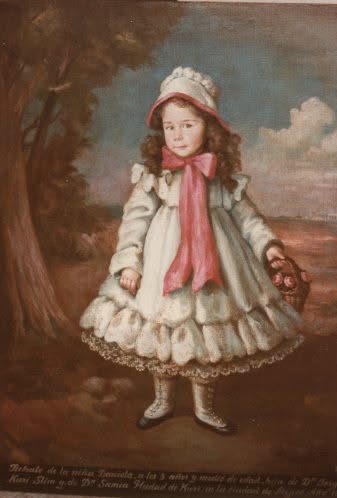 Niña con vestido blanco de volantes y cofia atada bajo la barbilla, con una canasta al brazo, al pie de un árbol